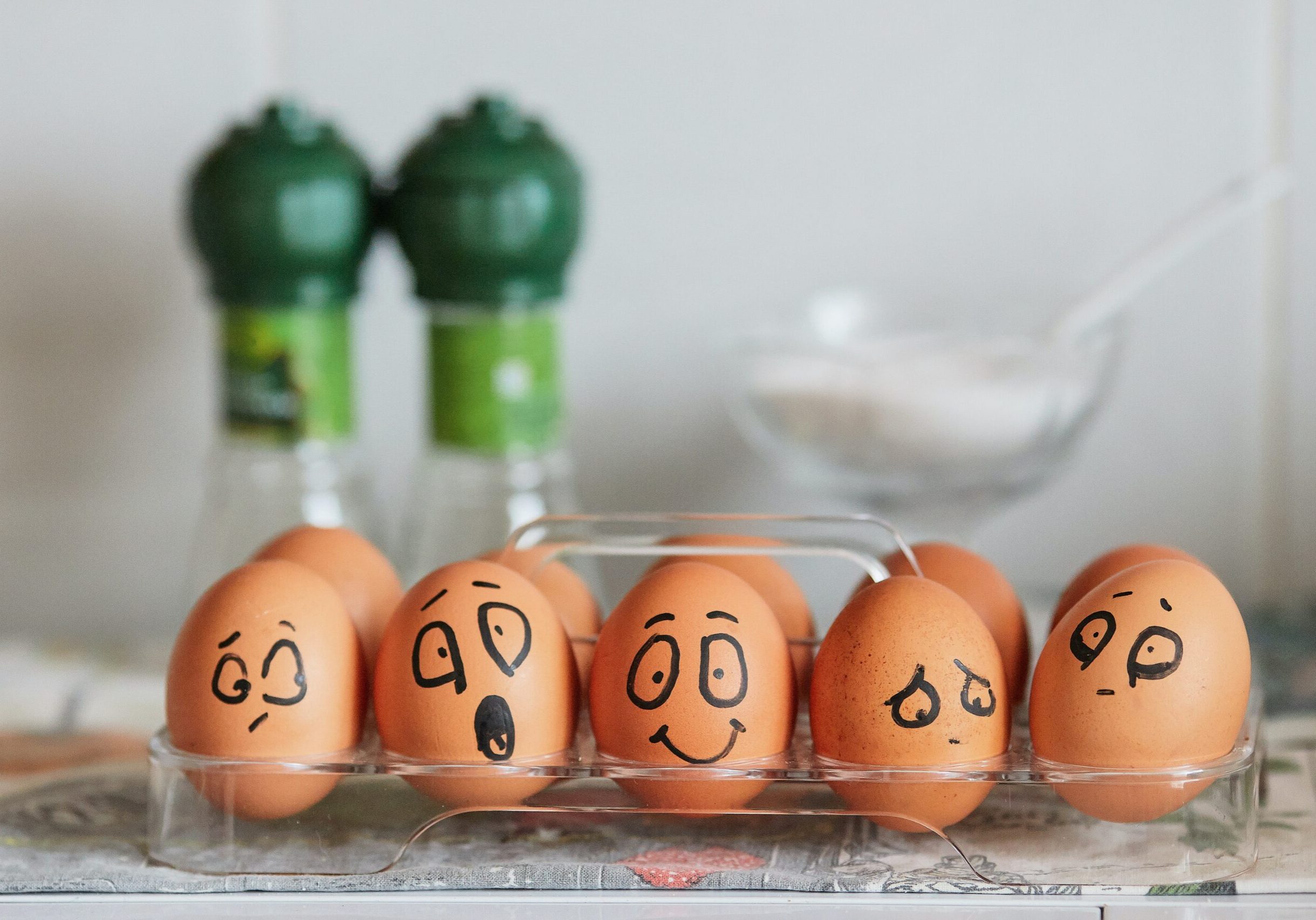 Im Vordergrund mehrere braune Eier mit aufgemalten Gesichern, im Hintergrund zwei grüne Salz- und Pfefferstreuer.